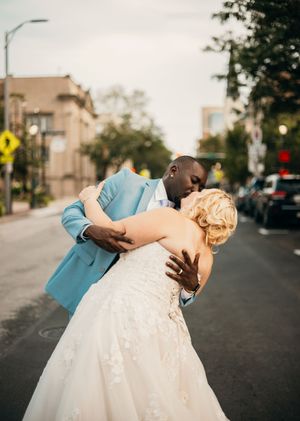 A romantic wedding couple in formal attire dips in an elegant dance pose on a city street at sunset.