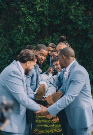 A group in light blue suits share a joyful moment together while gathered outdoors against green foliage.