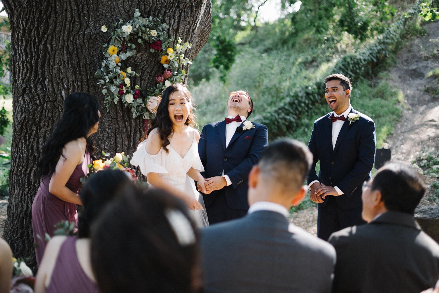 Amanda and William laughing during their outdoor wedding in the garden at Abbotsford Convent, Melbourne, surrounded by lush greenery.