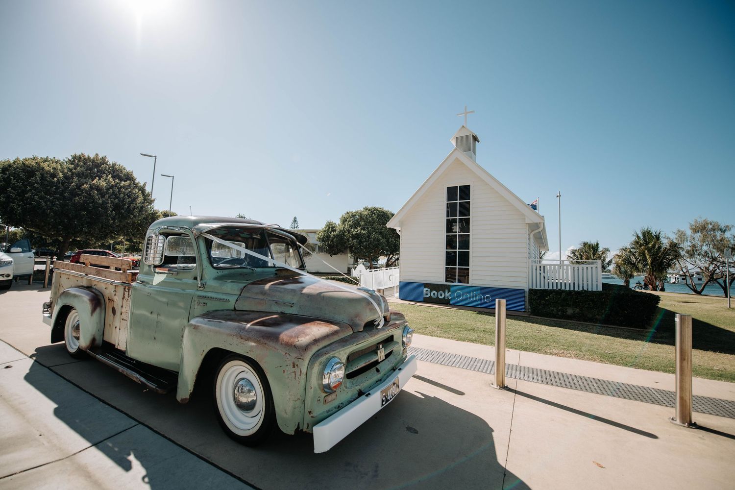 Vintage mint green pickup truck parked in front of a white chapel under blue sky.