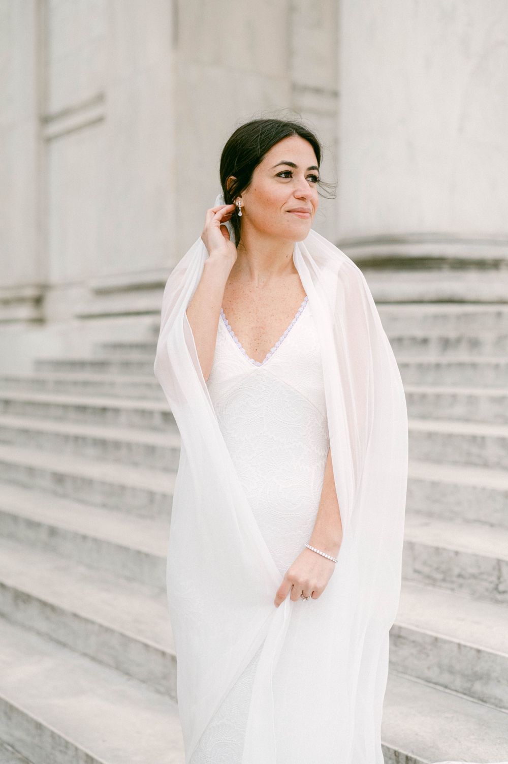Elegant bride in white gown and veil posing on marble steps.