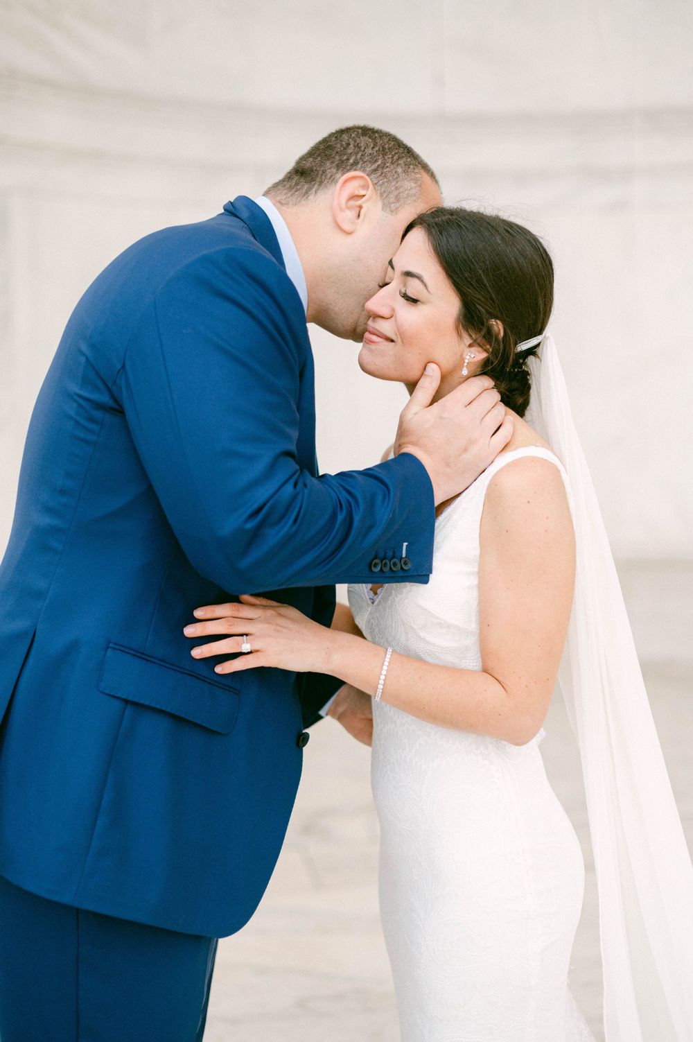 Tender moment between newlyweds against white marble background.