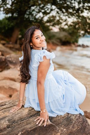 A child in a light blue dress poses on a rock formation at sunset, displaying a carefree and playful mood.
