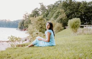 A couple sits together on a grassy hill overlooking a scenic lake on a sunny summer day.