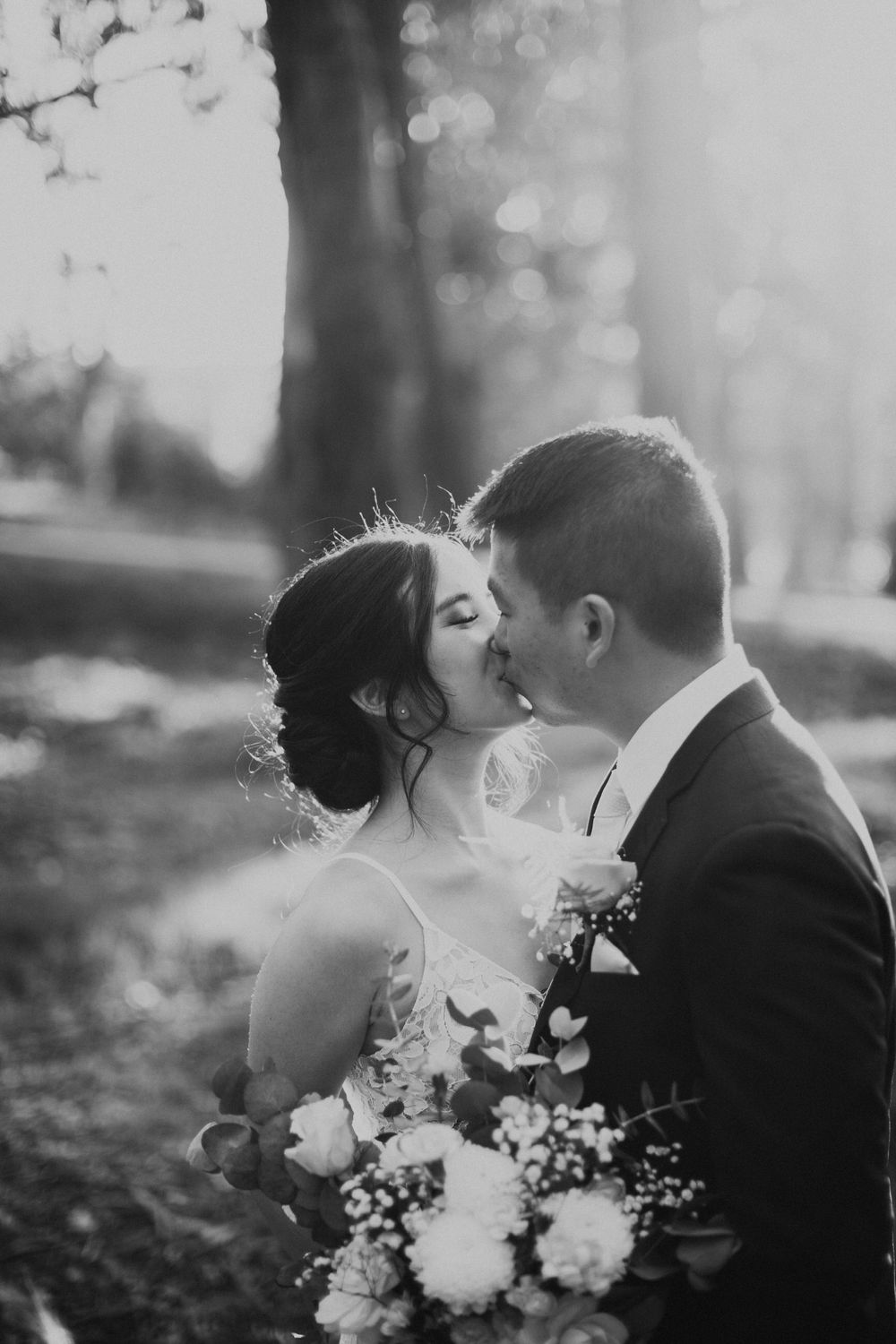 Black and white photo of wedding couple sharing intimate kiss while holding floral bouquet.