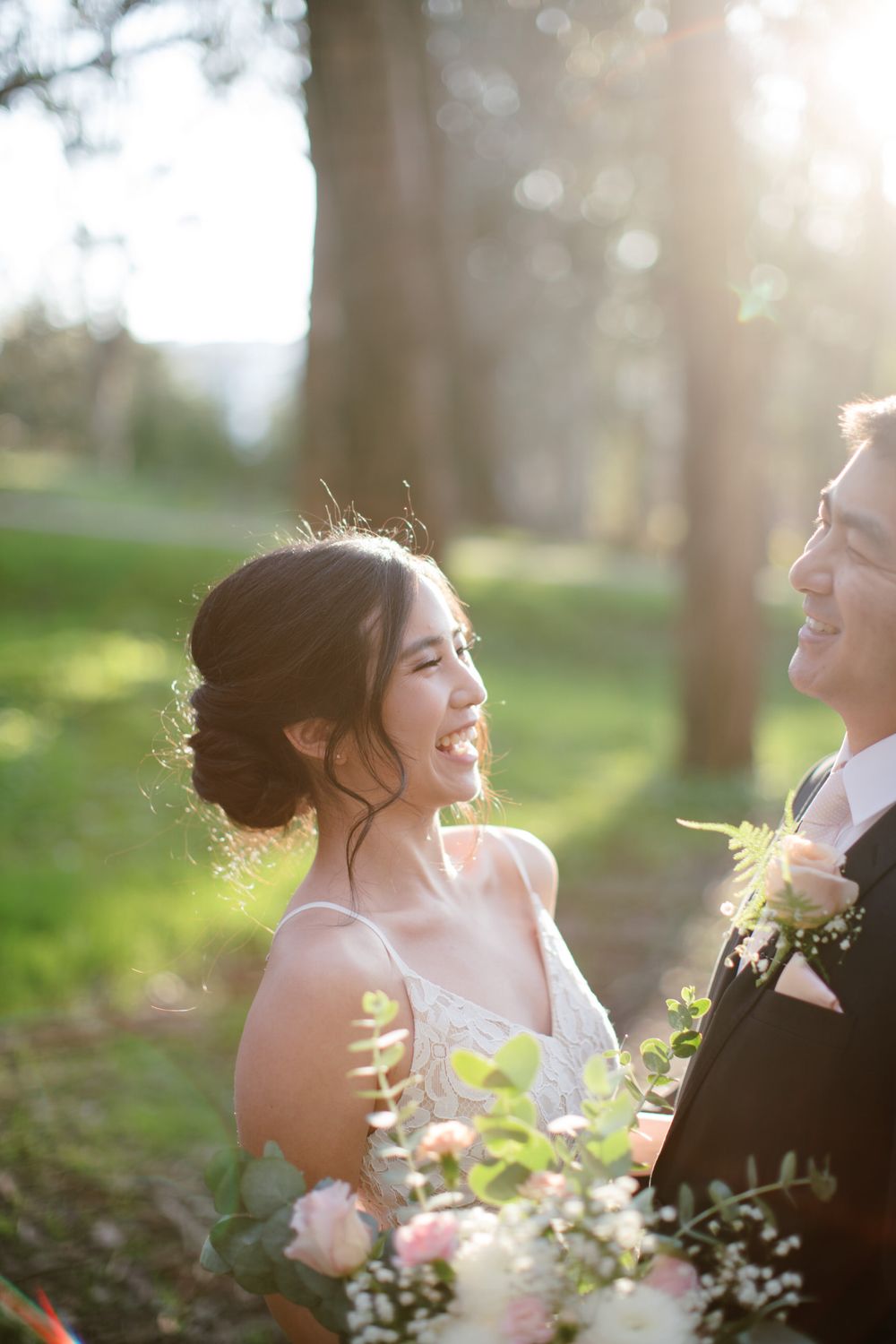 Sunlit wedding portrait with couple in formal attire holding bouquet in outdoor setting.