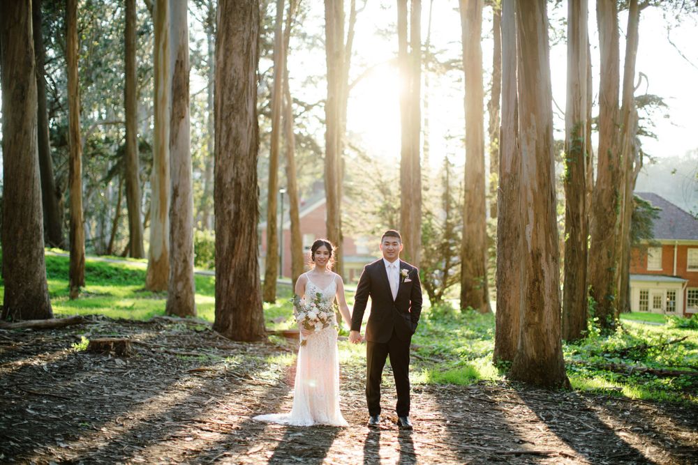 Wedding couple walking hand in hand through sunny forest with golden light streaming through trees.