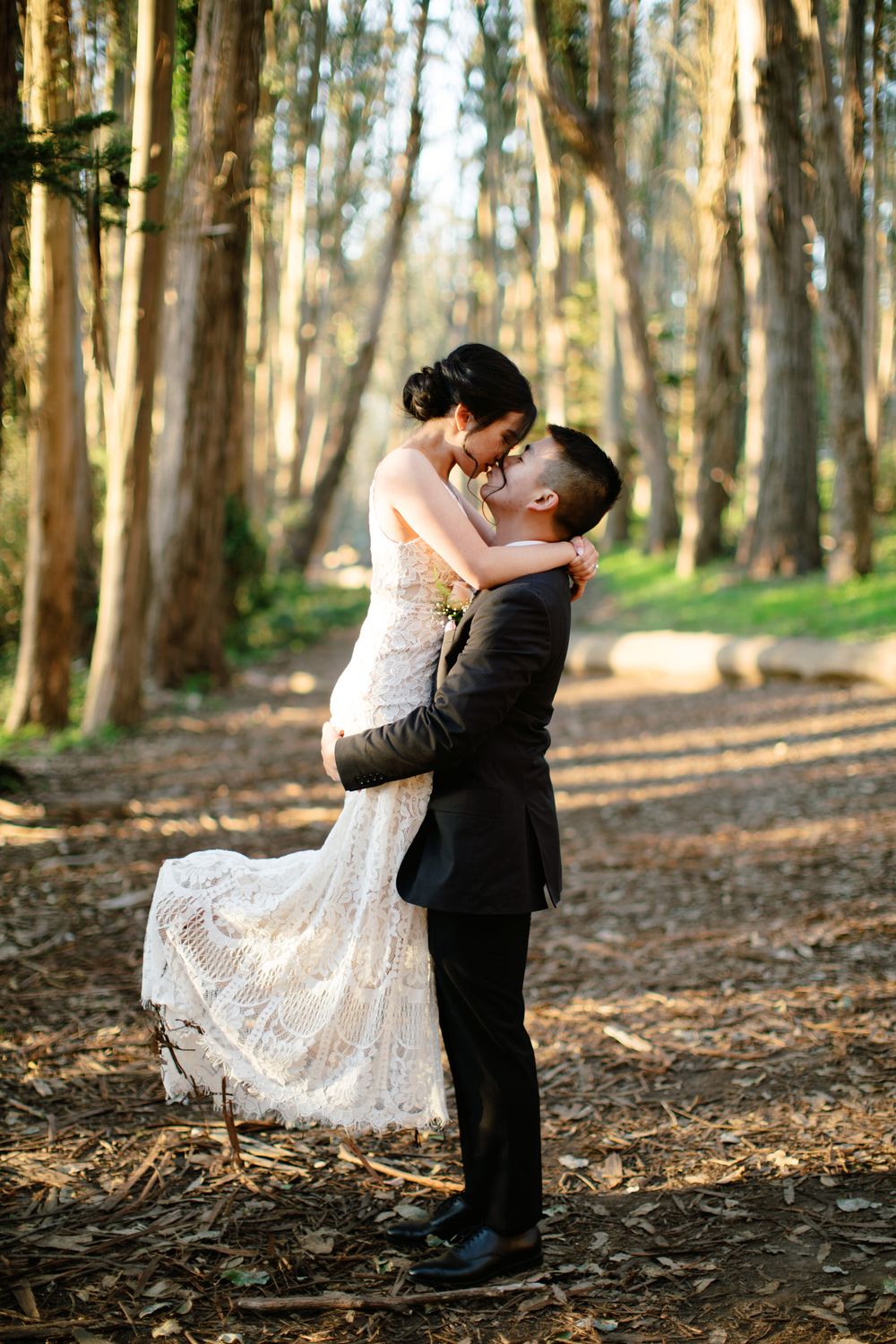 A romantic wedding photo of a couple embracing in a eucalyptus forest with the bride wearing a lace gown.