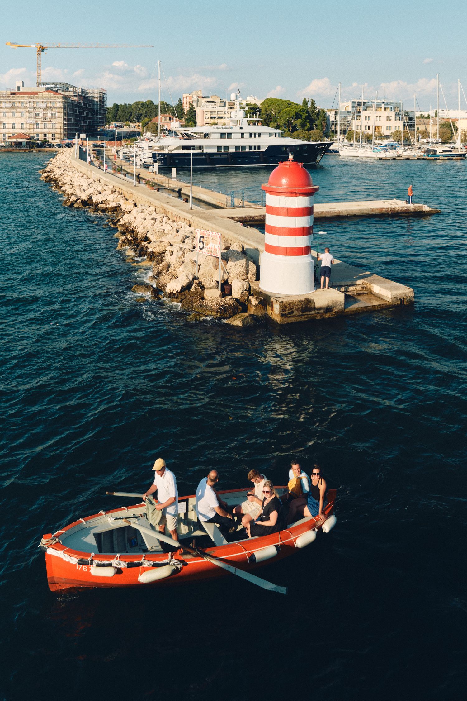 Small red and white lighthouse on a rocky pier with a boat carrying passengers in the foreground.
