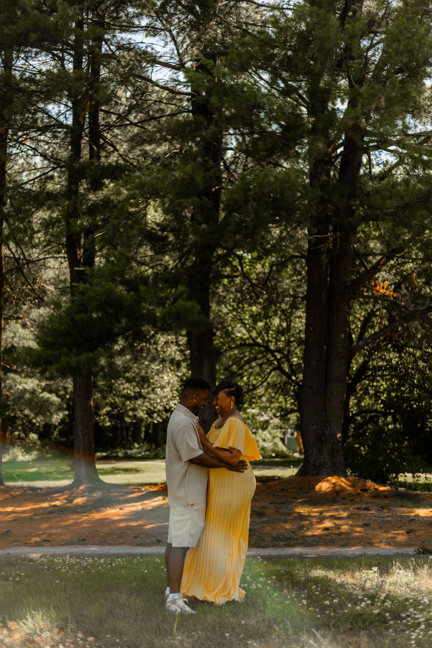 A loving couple shares a tender moment together in a sun-dappled forest setting wearing white and yellow outfits.