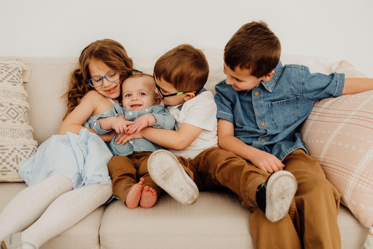 Three children sit together on a cream colored couch in casual clothing.