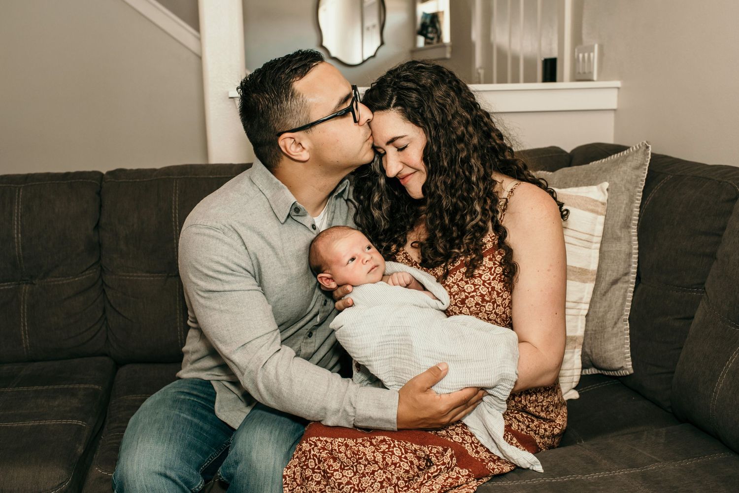 Intimate indoor family portrait with newborn baby on grey couch.
