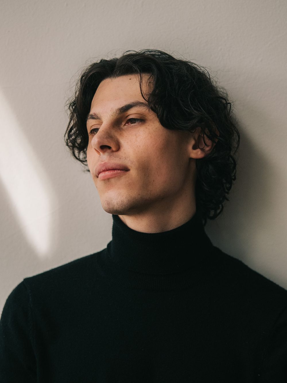 Artistic portrait series against neutral wall showing dramatic angles and shadows in moody lighting.