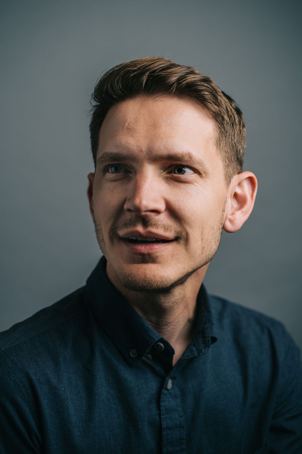 Professional headshot against gray background wearing navy blue collared shirt.