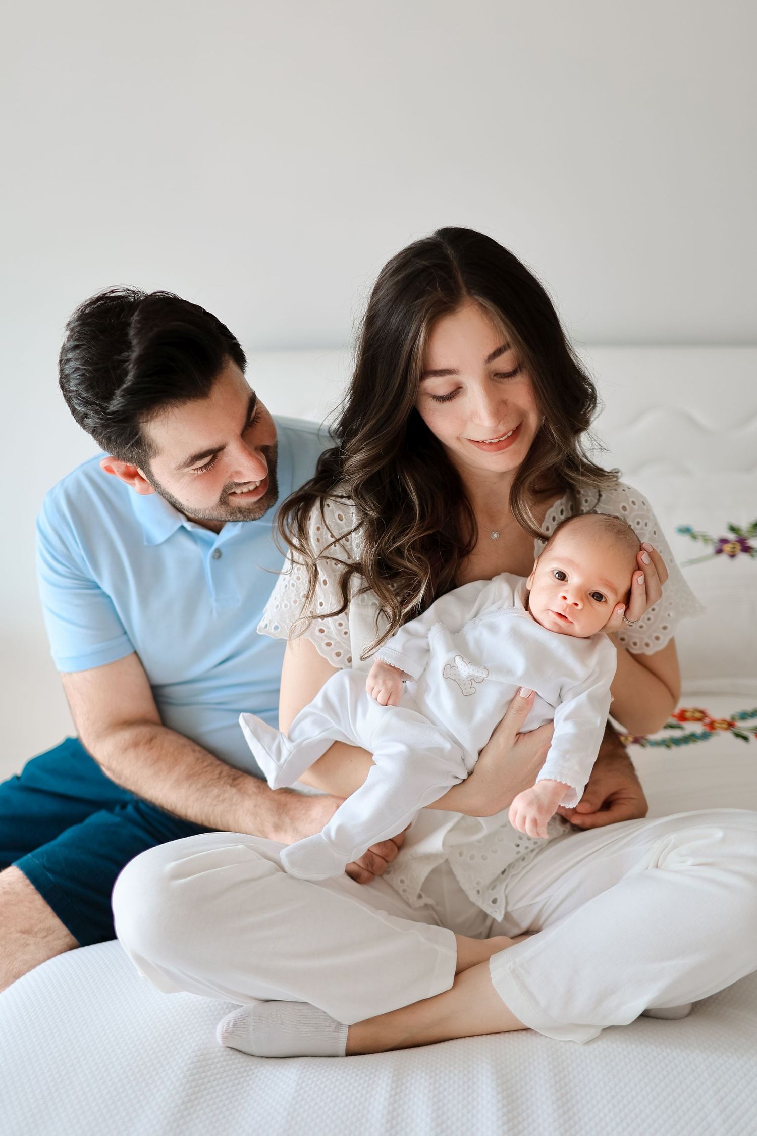 Happy family sharing a loving moment on white bedding with their infant in matching outfits.