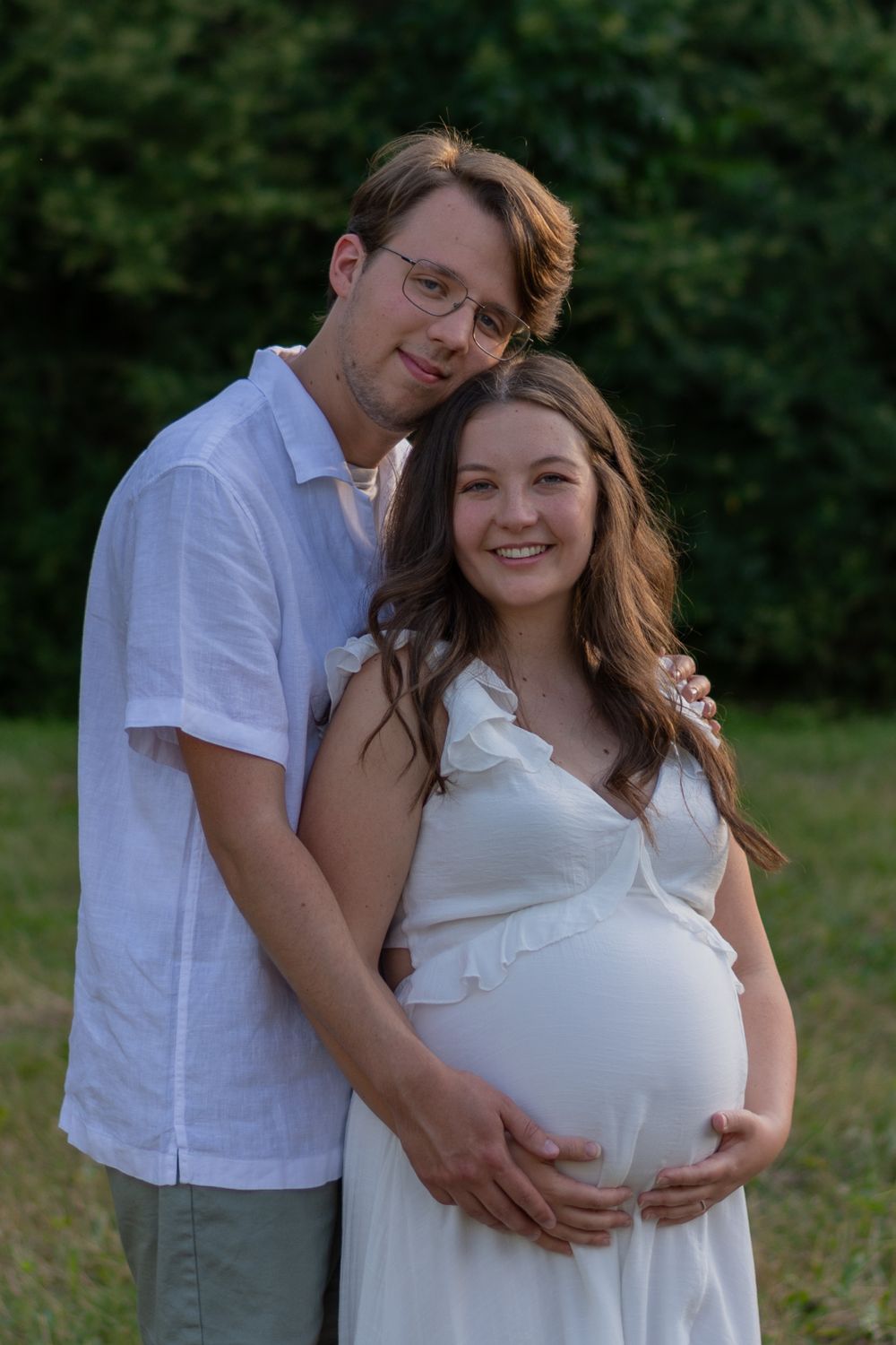 A more traditional pose of a couple during a maternity photo session in Fort Worth. She holds her baby bump as he stands behind her.