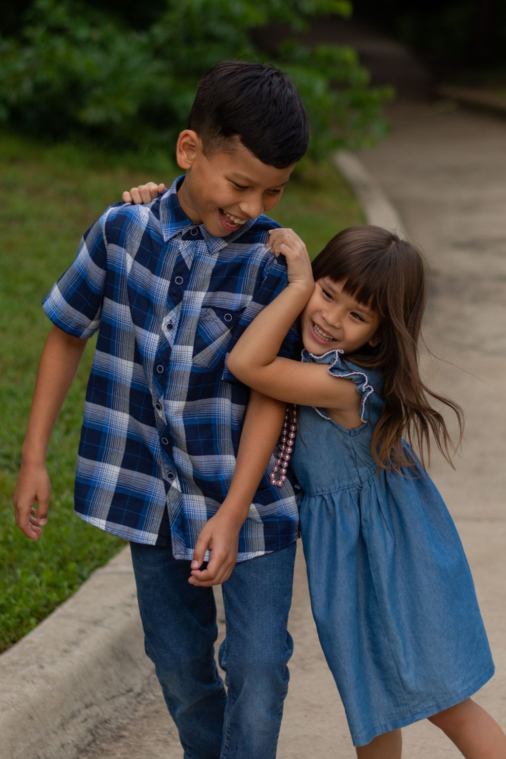 A young girl laughs as she hangs onto her older brother's shoulders, making him also laugh, during a Fort Worth family session at a park.