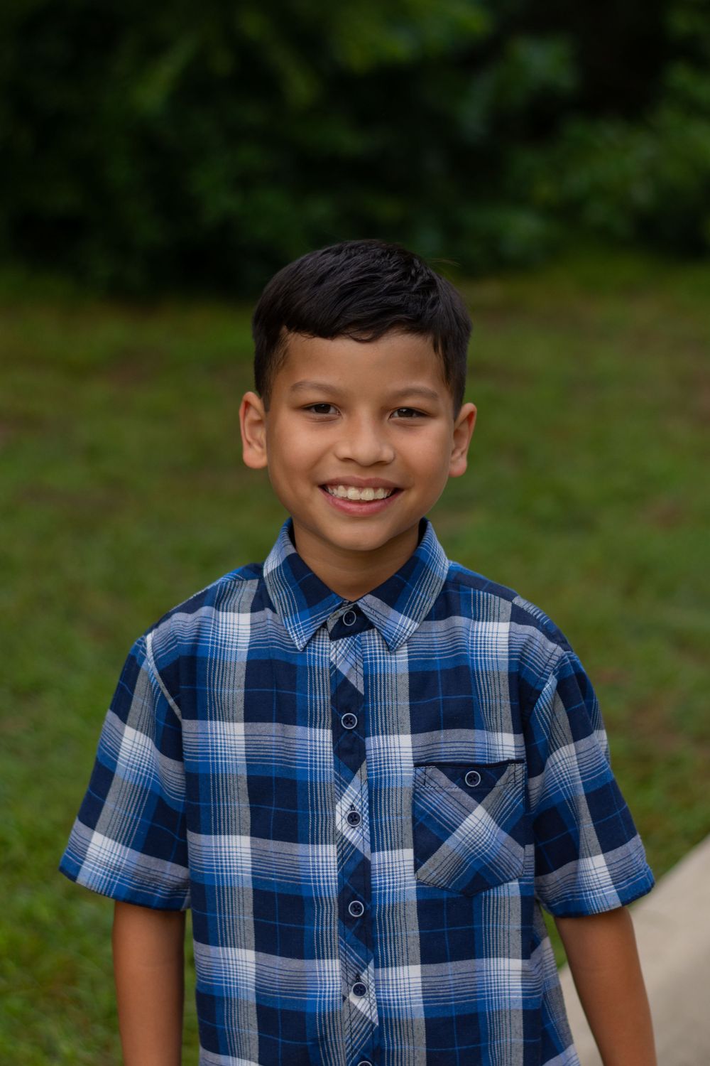A young boy smiles at the camera during a family's portrait photo session in Fort Worth at a park.
