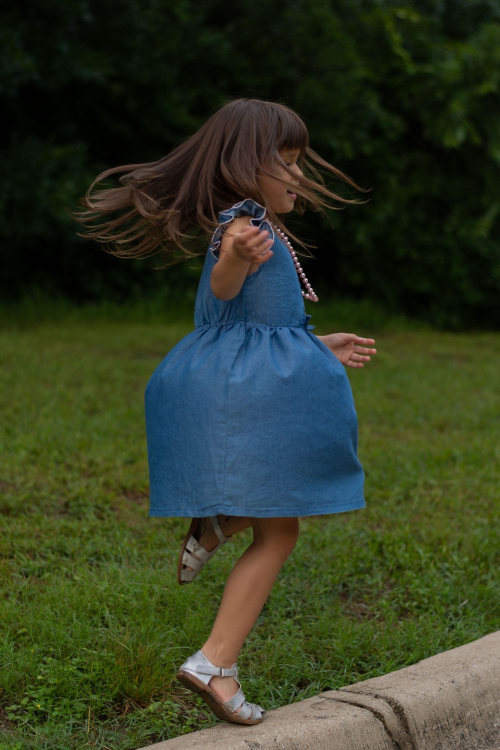 A young girl spins and twirls in her denim dress and pink pearls, hair flowing, during a candid family photo session moment in Fort Worth.