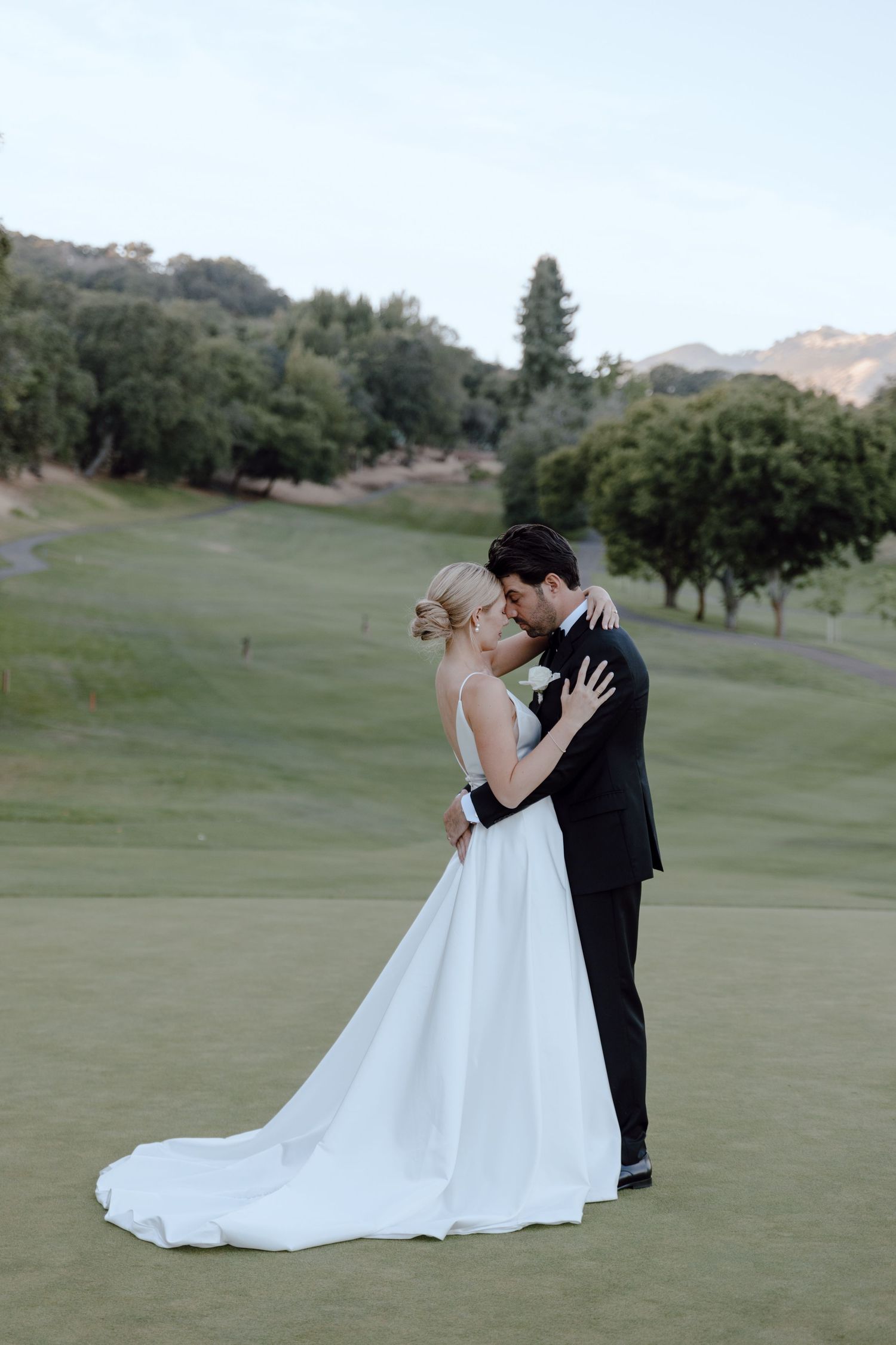 Wedding couple embracing on a pristine golf course with rolling hills in the background.