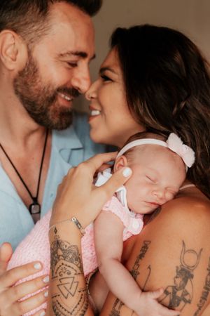 Intimate family portrait with tattooed parents cuddling their sleeping newborn in pink.
