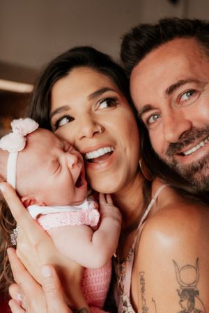 Joyful family portrait with sleeping baby in pink outfit and white bow.