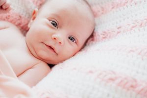 Close-up photo of an infant laying on pink and white patterned bedding.