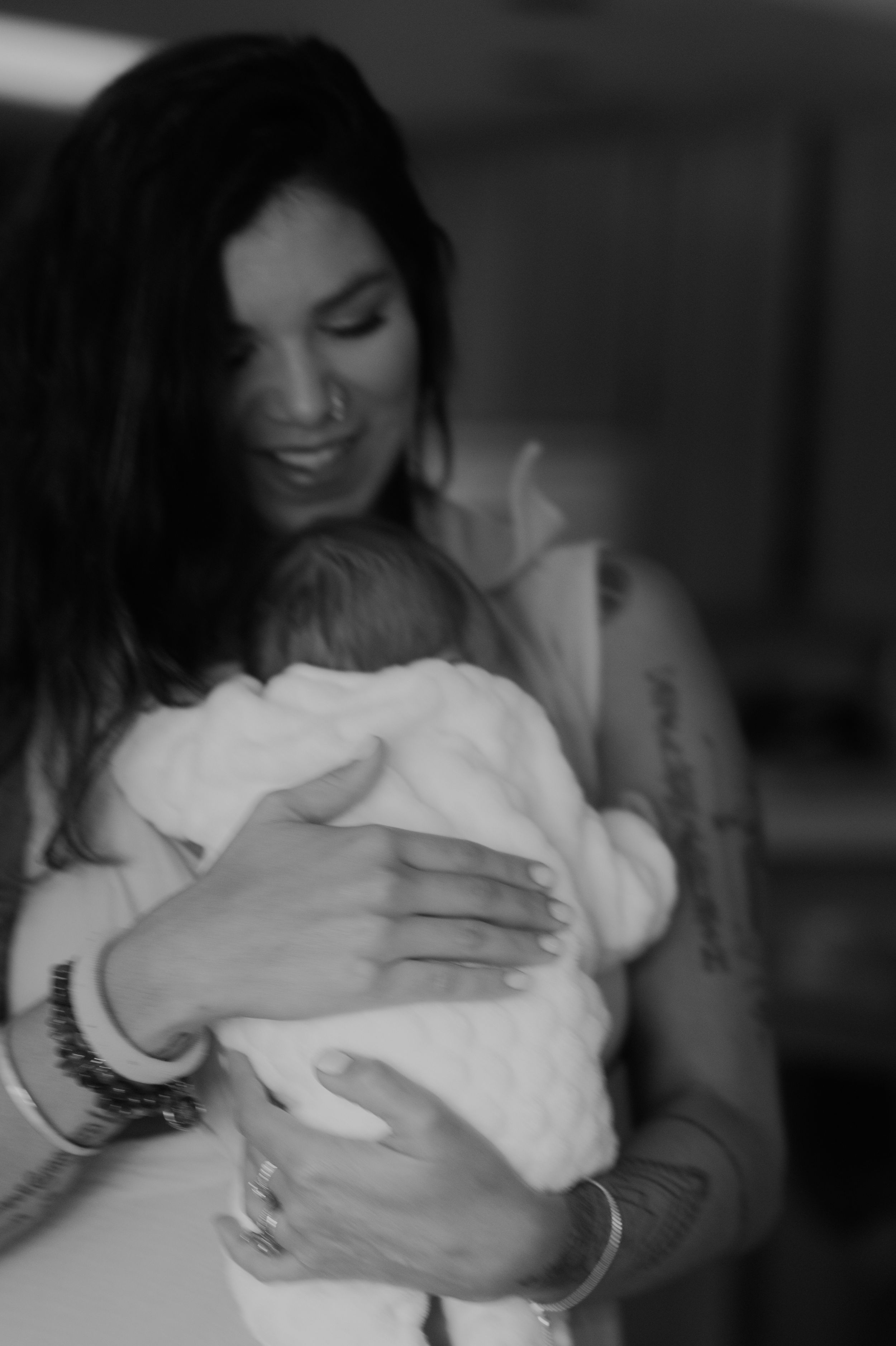 Person holding a newborn baby swaddled in white cloth in a dimly lit room.