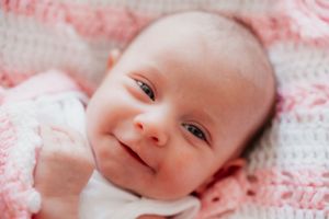 Sweet portrait of a smiling baby on pink and white blankets.