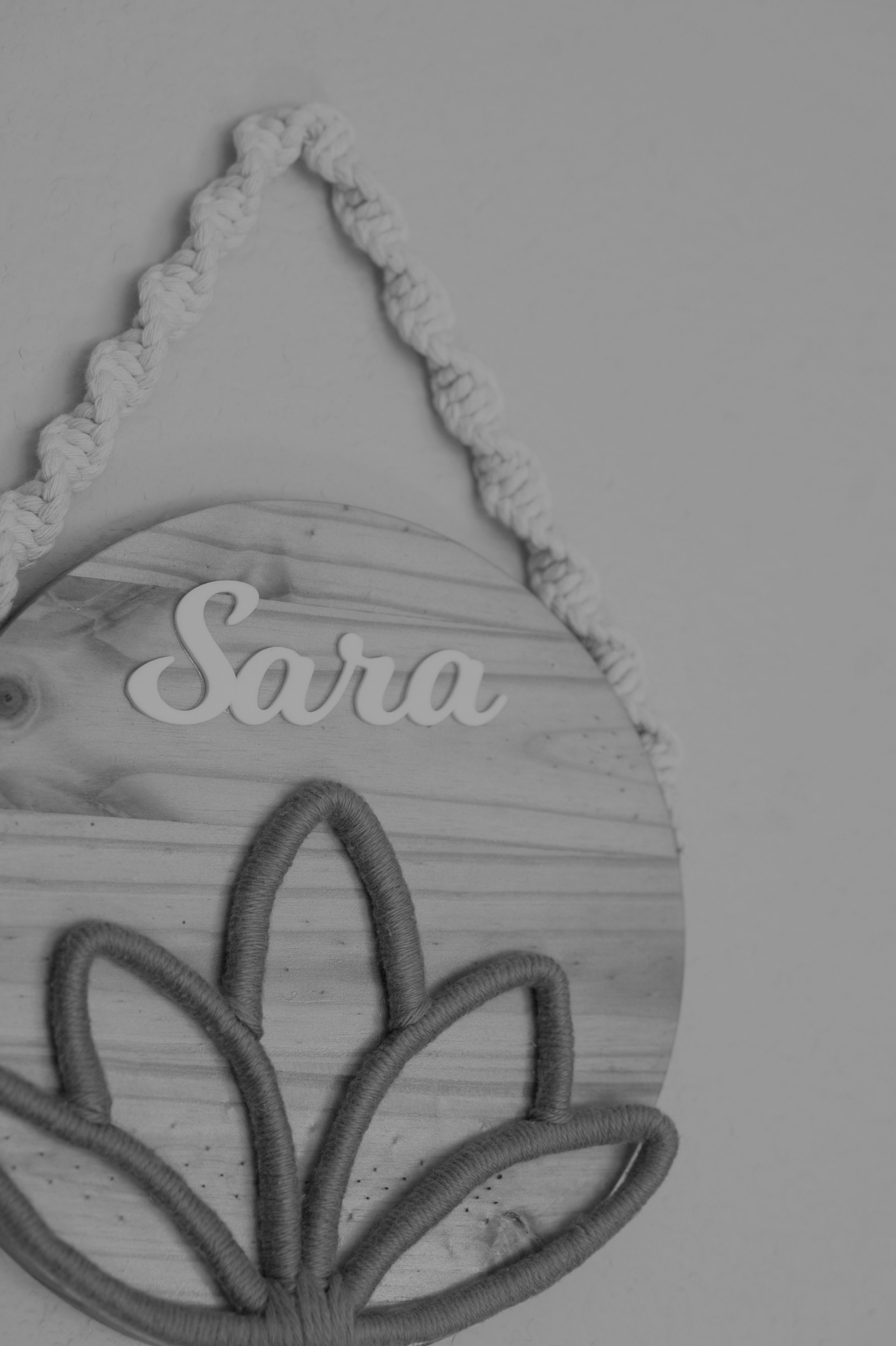 Wooden decorative sign with 'Sara' text and floral design hanging from braided rope.