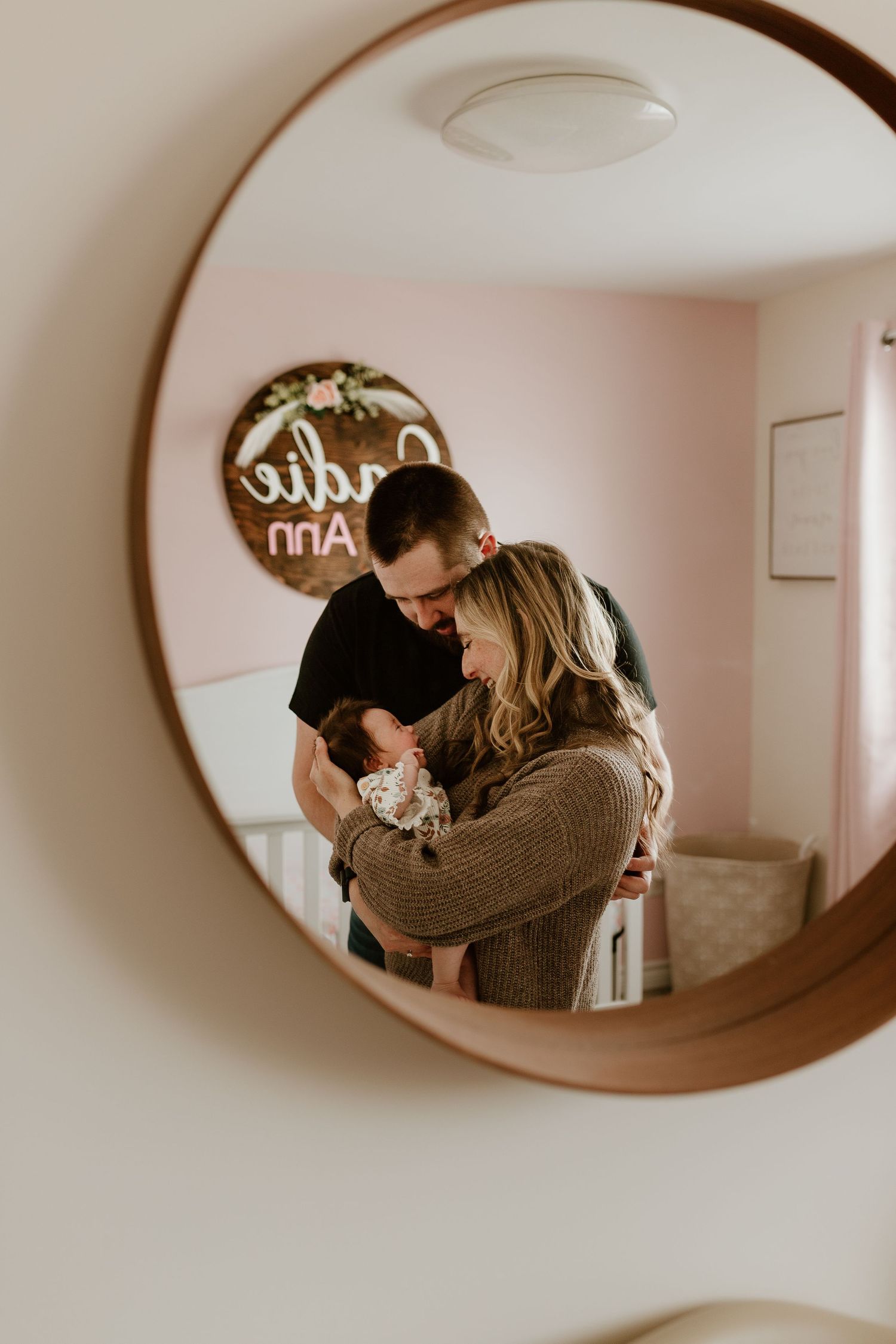 A loving new mom and dad holding their baby daughter, view through the nursery mirror