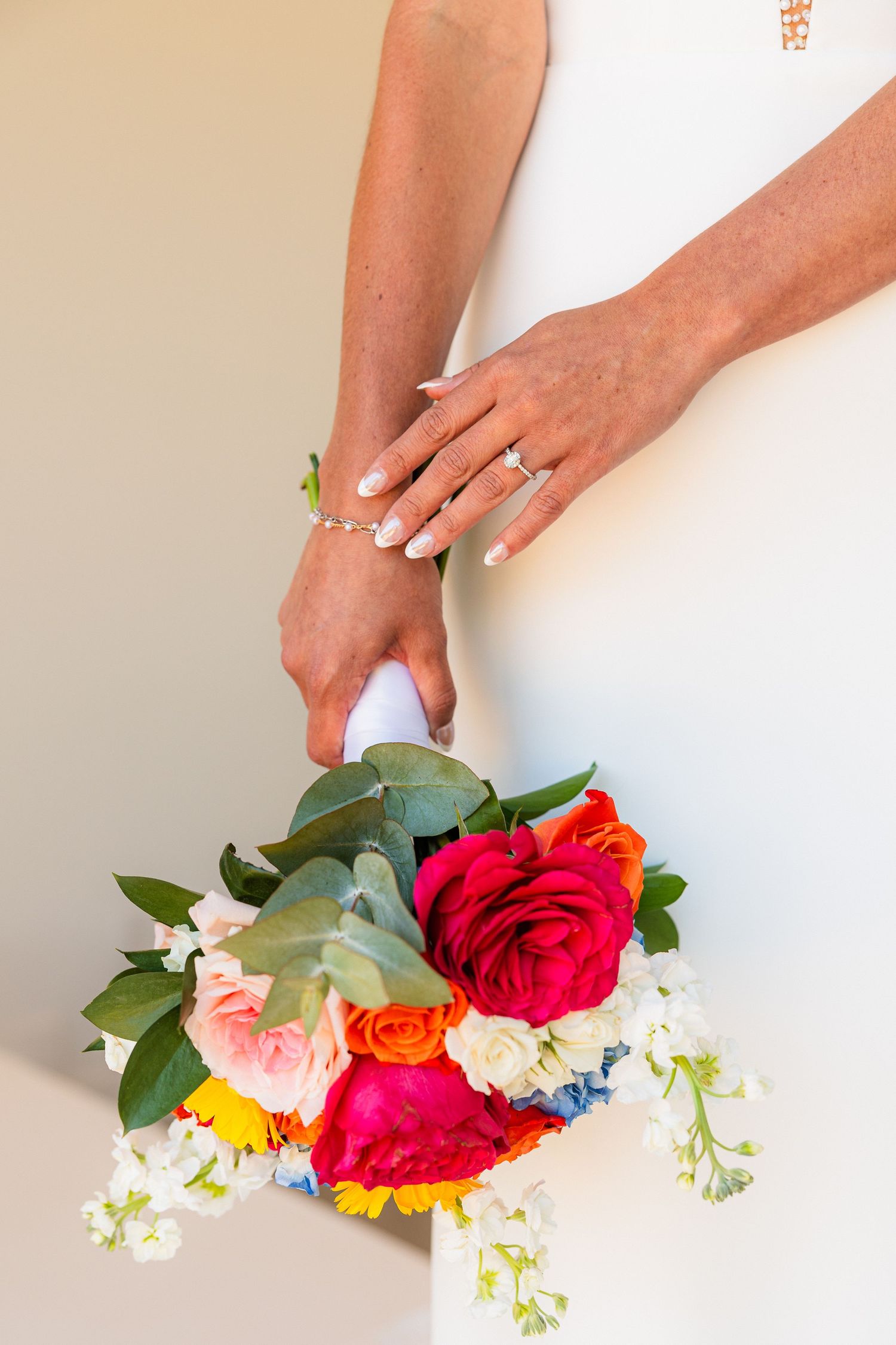 Close-up of bridal jewelry and colorful wedding bouquet against white background.