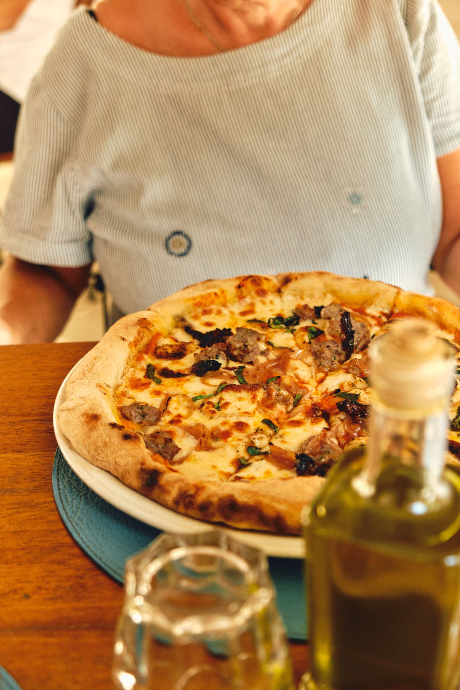 Fresh wood-fired pizza with mushrooms and cheese served on blue plate with olive oil bottle.