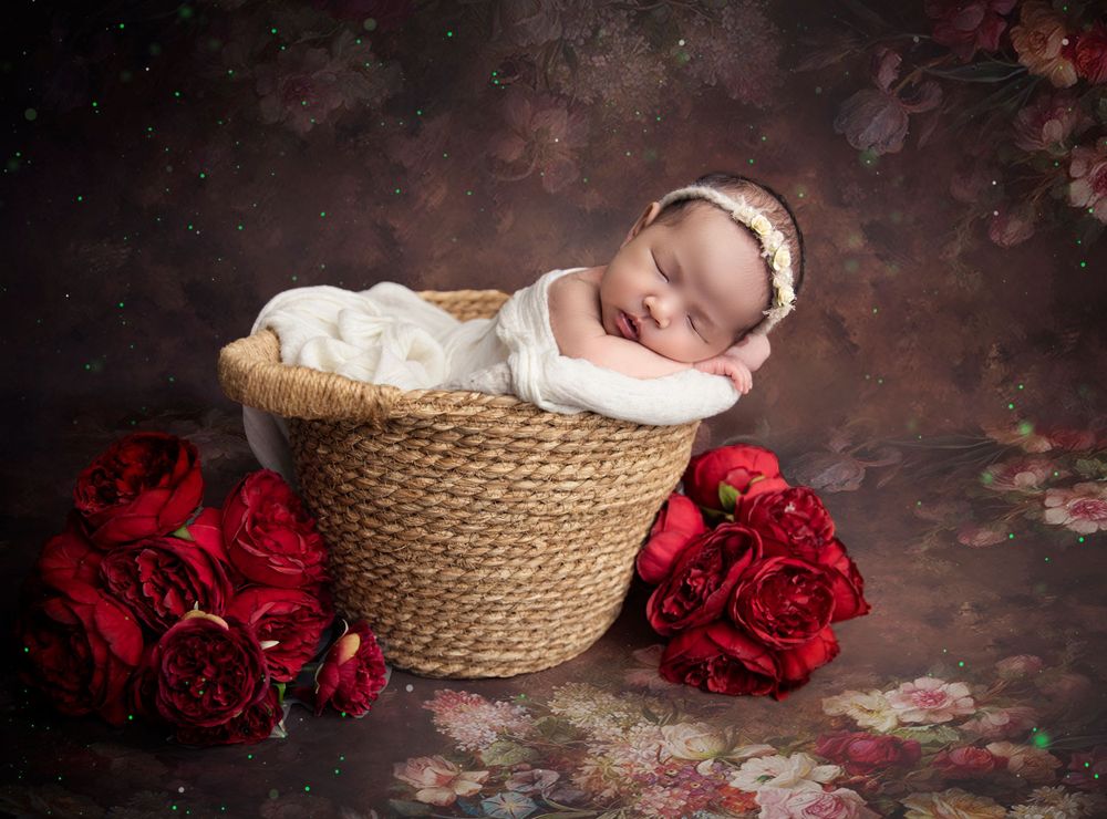 Peaceful sleeping newborn in basket with red roses against dark rustic backdrop.