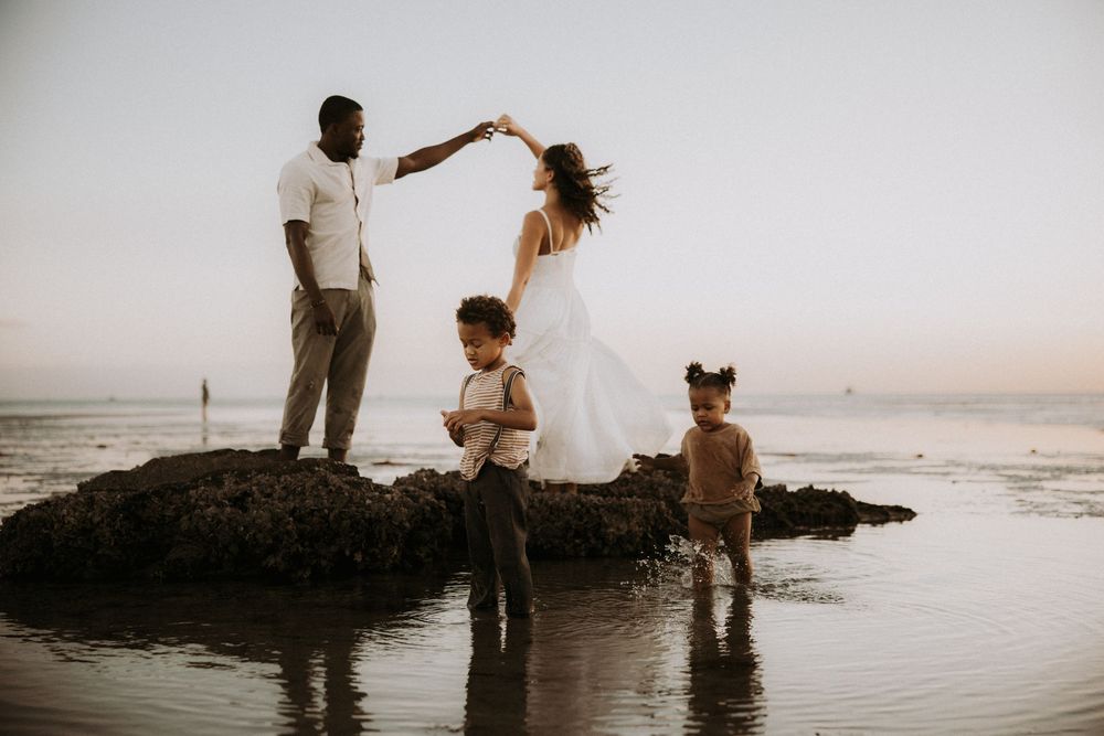 Romantic couple sitting on coastal rocks during sunset at the beach with waves crashing in the background.