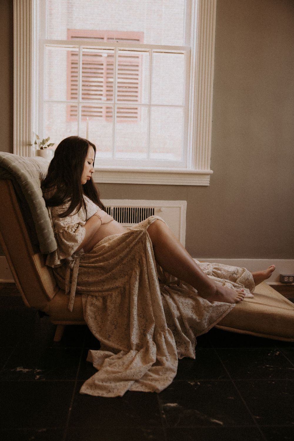 A person in a cozy brown sweater lounges on a window seat in a moody, dimly lit room.