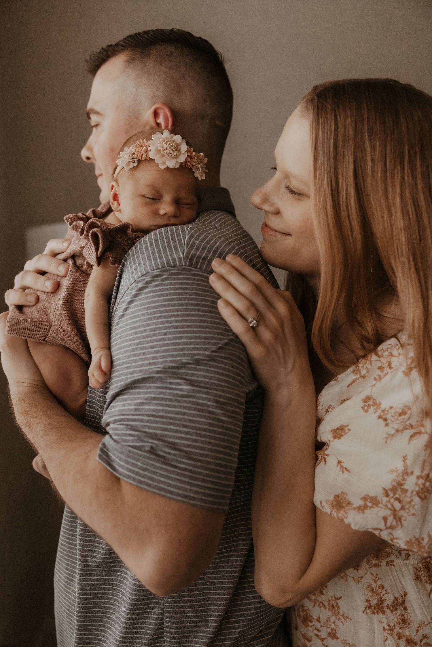 Parents tenderly holding their newborn baby girl wearing a floral headband in a warm, intimate family portrait.