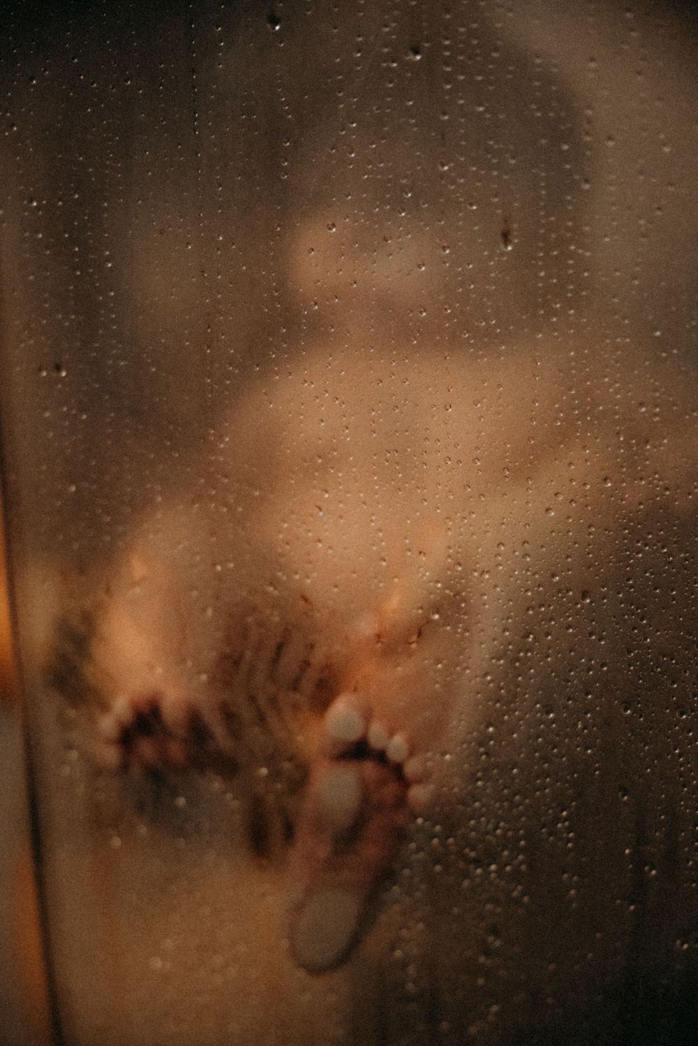 Blurred silhouette of a person behind a wet glass shower door with water droplets.