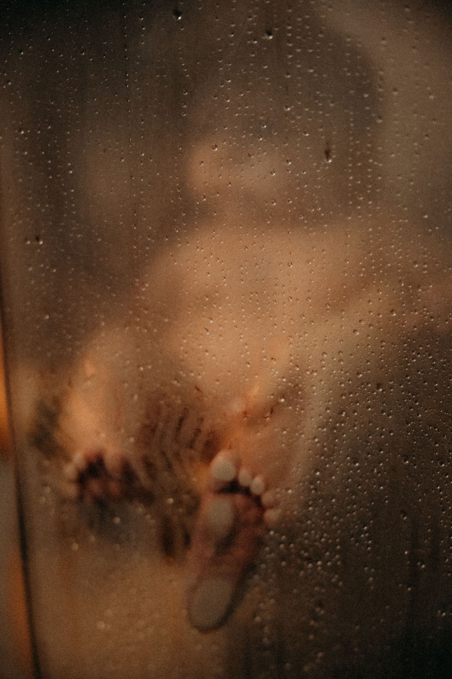 Blurred silhouette of a person behind a wet glass shower door with water droplets.