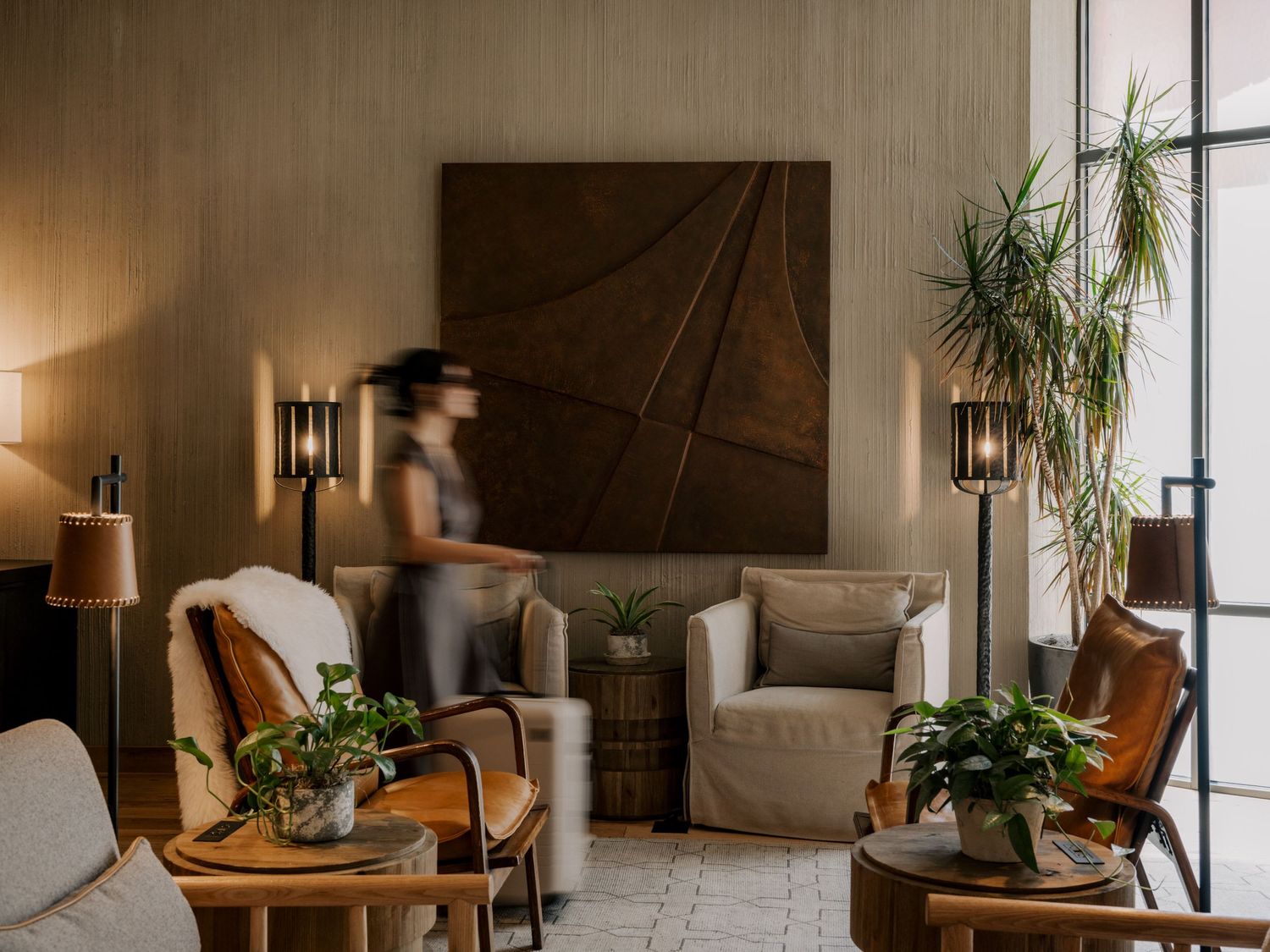 Modern living room with blurred motion, featuring brown wall art, potted plants, and mid-century furniture in warm lighting.