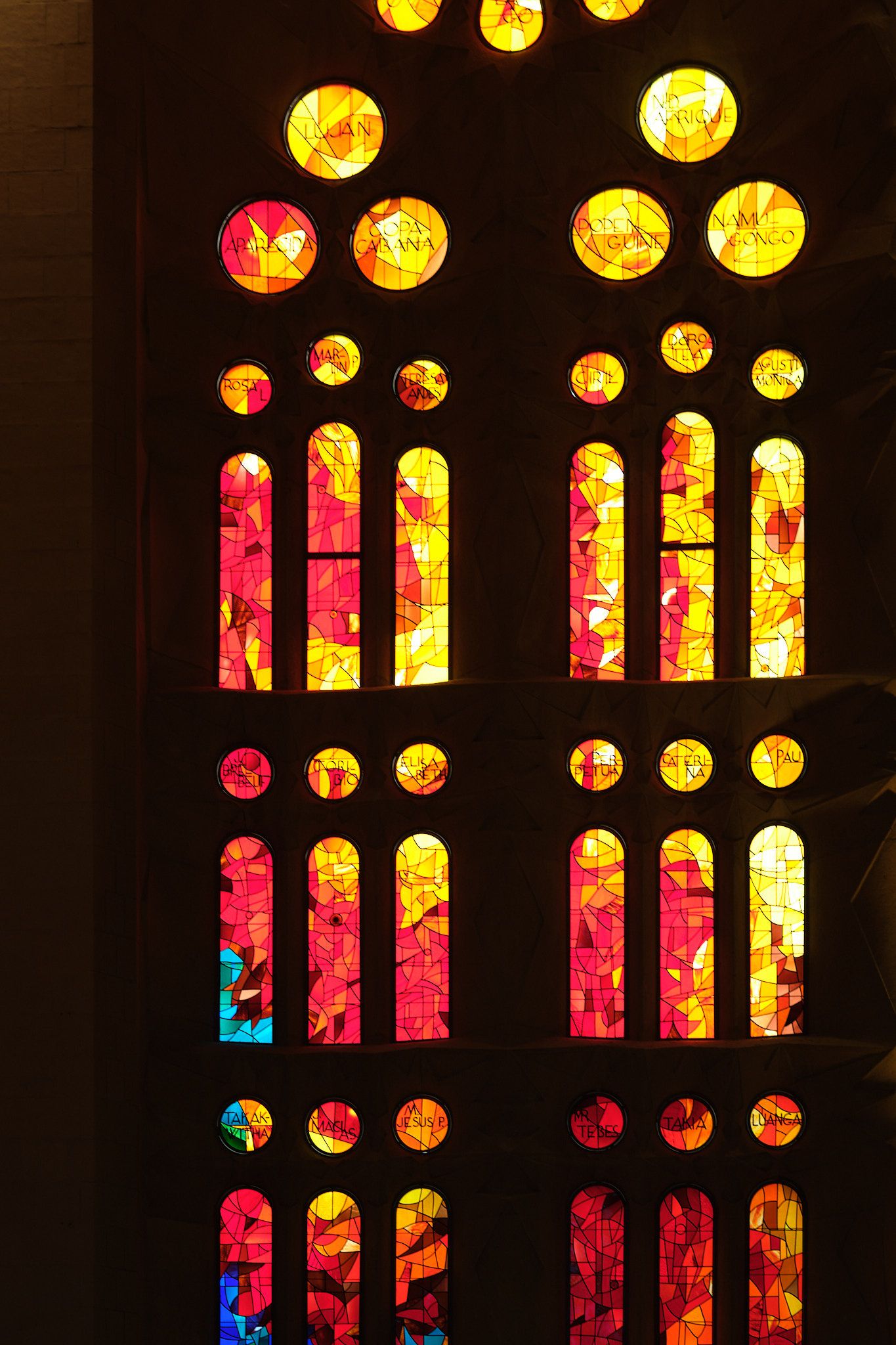 Vibrant stained glass windows in warm red, orange, and yellow hues with circular and arched panels in a cathedral.