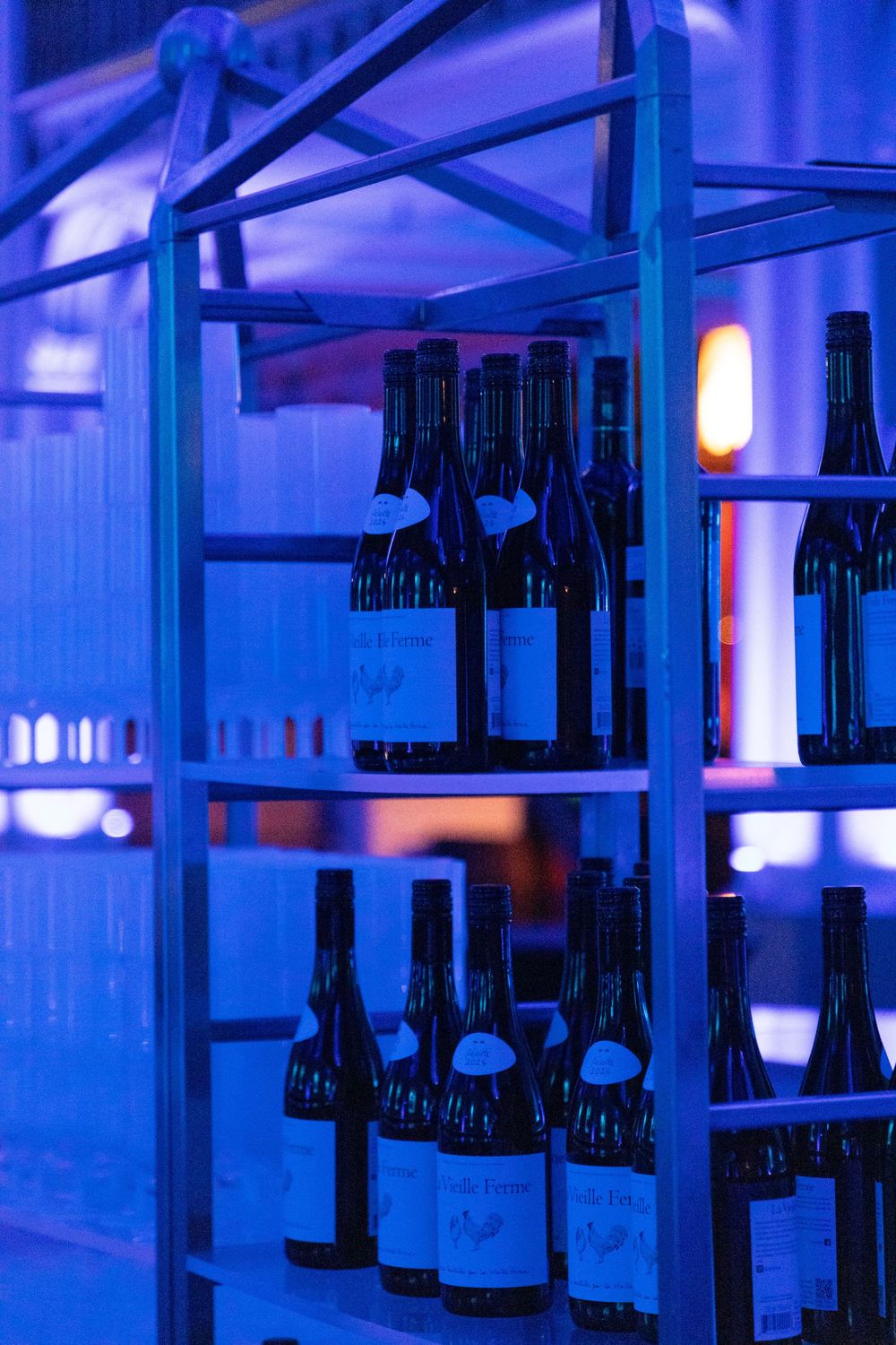 Dark wine bottles line illuminated blue shelves in a modern bar or cellar display.