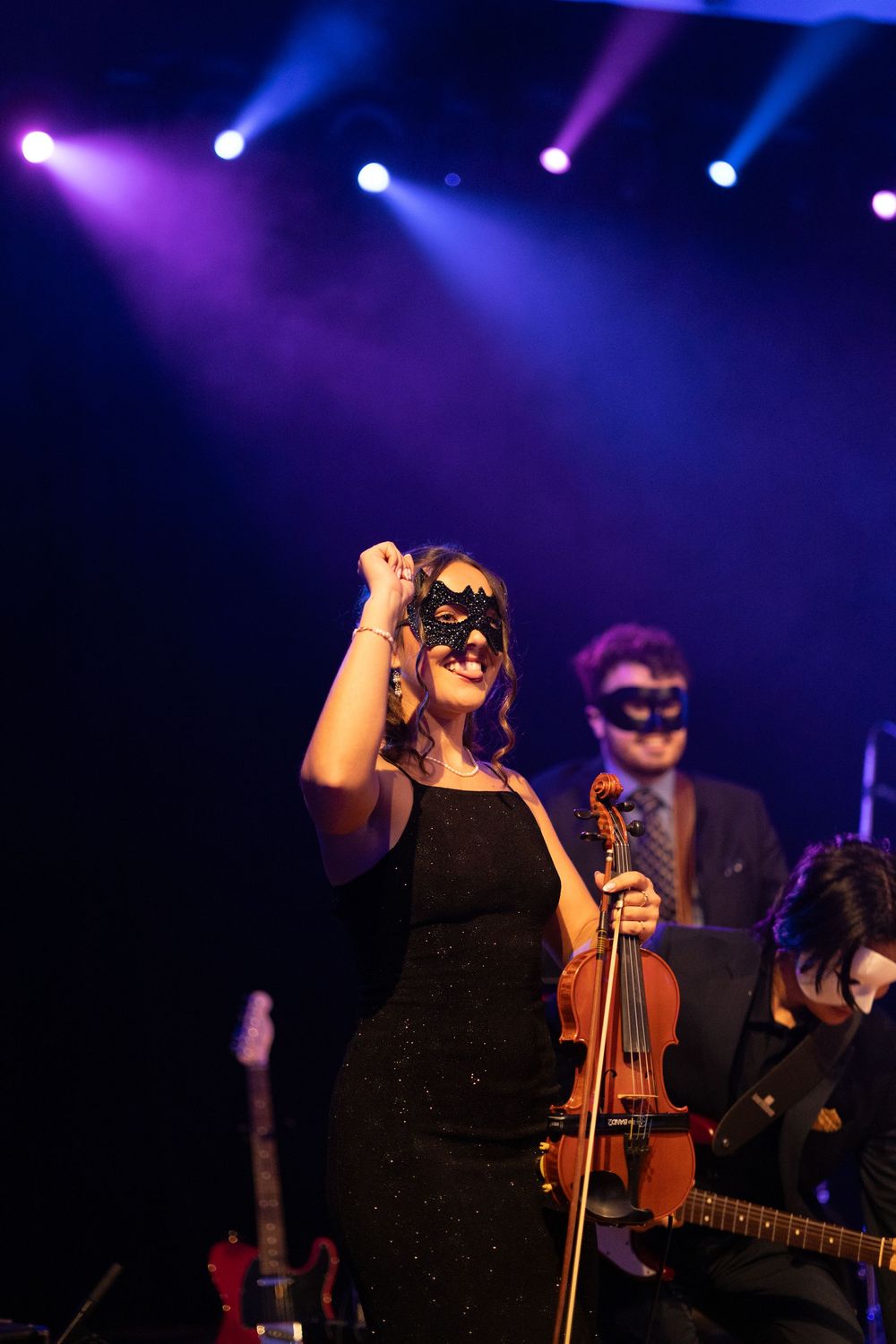 Musicians performing on stage with dramatic purple and blue concert lighting creating a moody atmosphere.