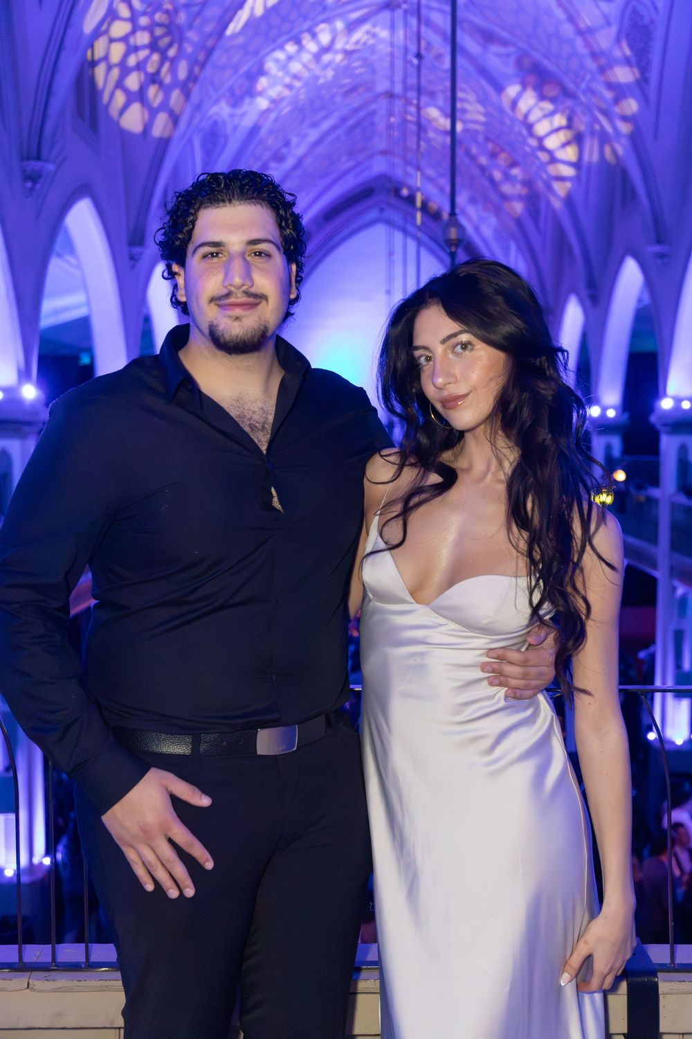 Guests posing at an elegant event venue with blue uplighting and gothic architectural details.