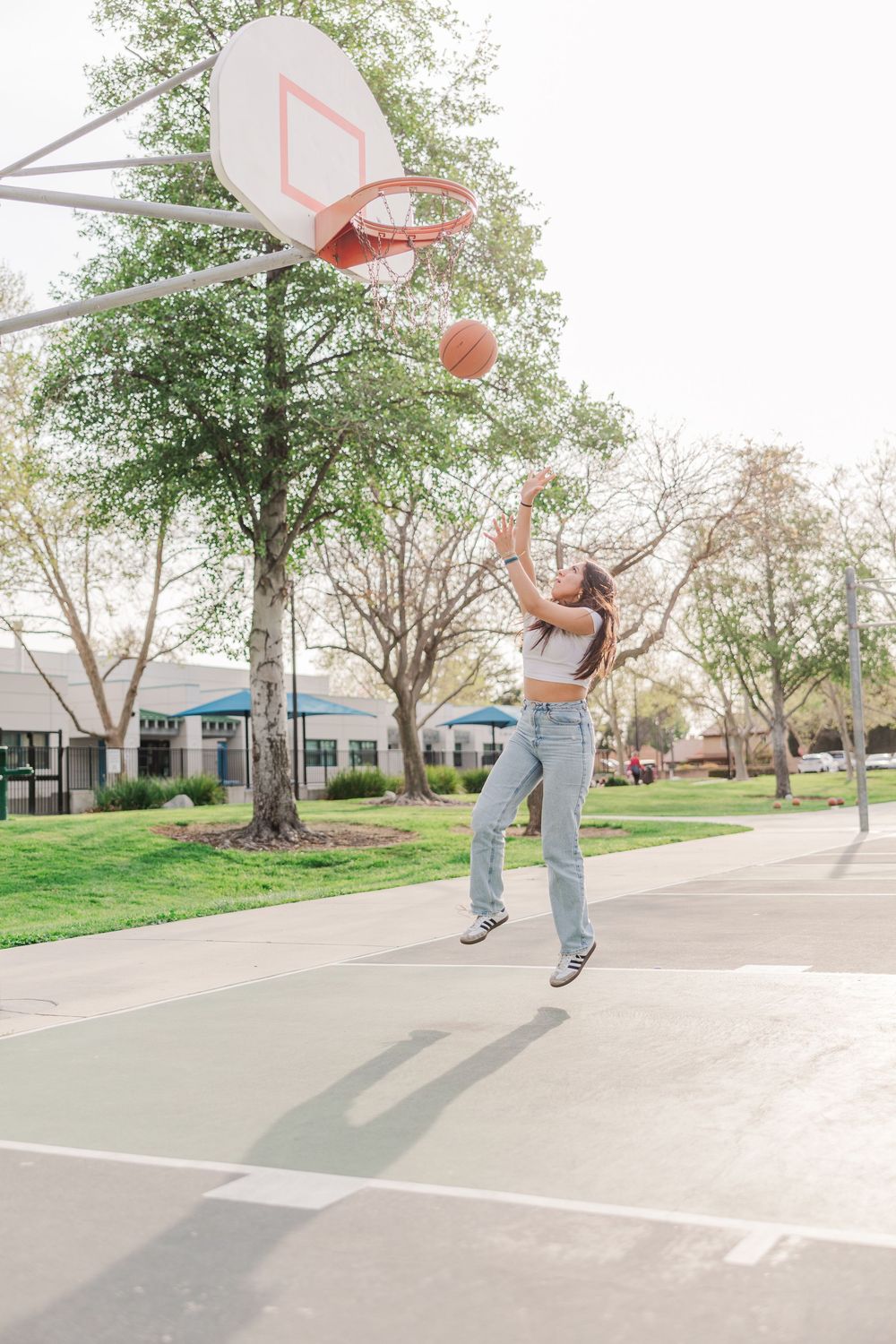 Athletic person shooting basketball on outdoor court by jumping and aiming for the hoop.