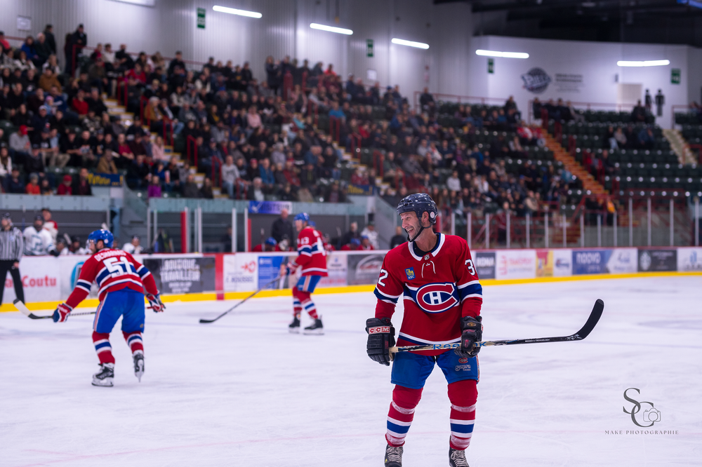 Hockey player in red uniform stands ready on ice during game with crowd in background.