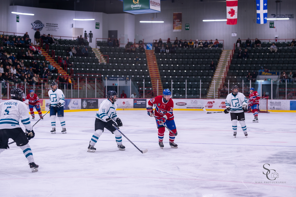 Hockey match in progress with Canadian and Quebec flags visible in arena above players.