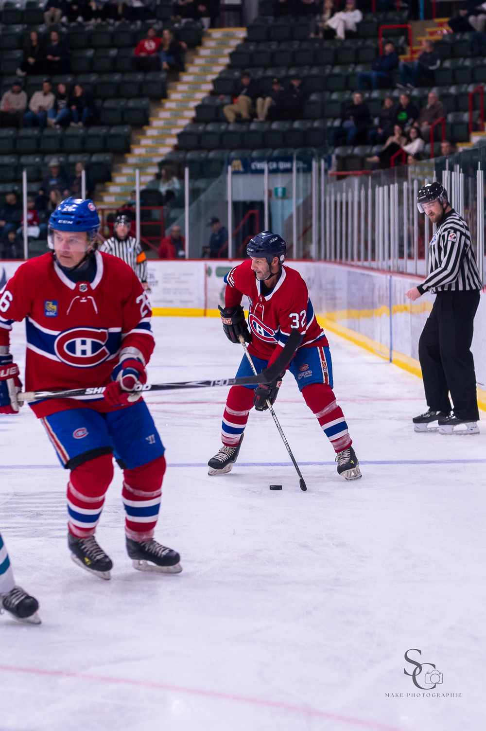 Montreal Canadiens players in red uniforms control the puck while referee observes.