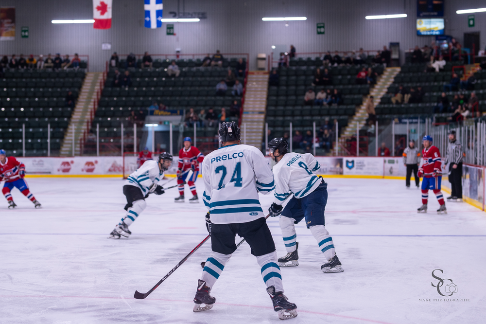 Hockey players in white jerseys position themselves during competitive game action.