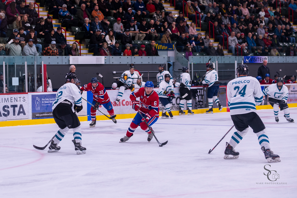 Hockey players face off on the ice during a competitive game between red and white uniformed teams.